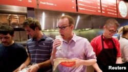 FILE - Steve Ells, center, CEO of Chipotle Mexican Grill, eats a burrito at a New York Chipotle restaurant. The chain's loaded chicken burrito contains 2,790 mg of sodium.