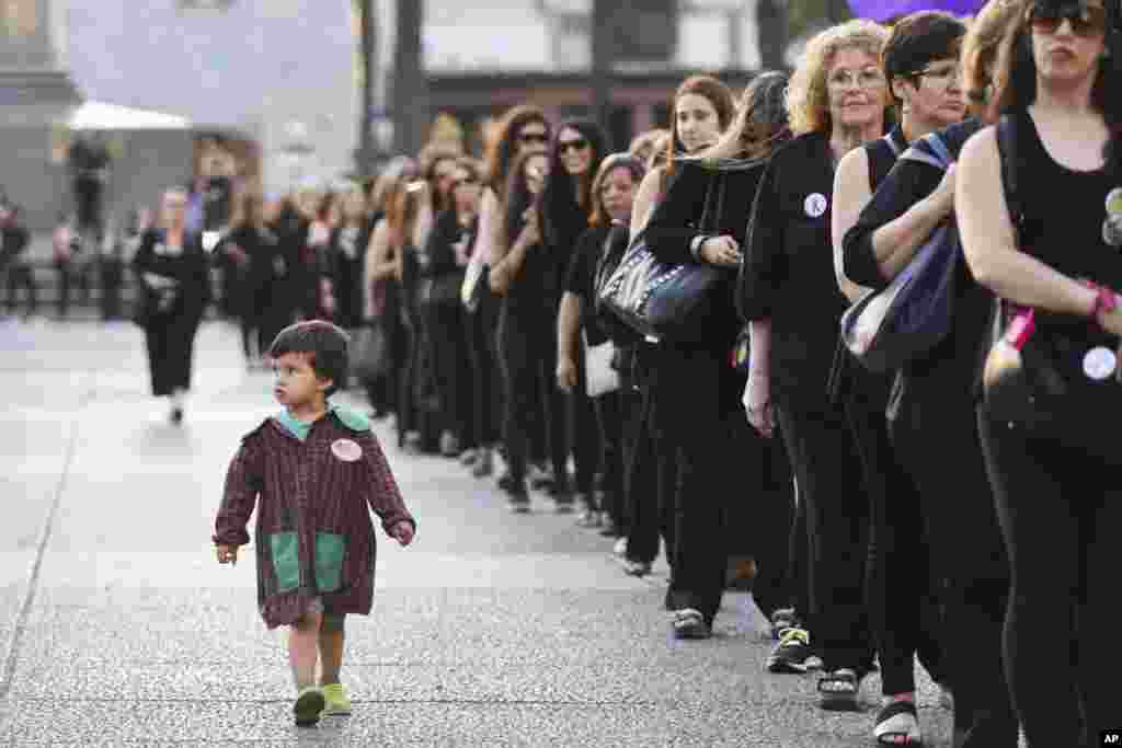 Seorang anak laki-laki melihat barisan orang berpakaian hitam yang berdemonstrasi dalam peringatan Hari Internasional untuk Penghapusan Kekerasan Terhadap Perempuan di Montevideo, Uruguay (25/11). (AP/Matilde Campodonico)