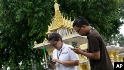 Thai reporters play Pokemon Go on their phone in front of a spirit house at a Government building in Bangkok, Thailand, Aug. 8, 2016. 