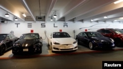 FILE - Tesla Model 3s and X's are shown charging in an underground parking lot next to a Tesla store in San Diego,California, May 30, 2018.