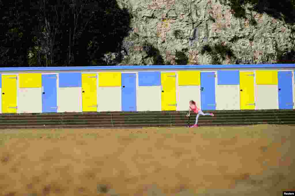A youngster scooters passes beach huts along the promenade as the sun shines in Broadstairs, southern England.