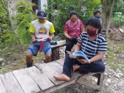 Sekelompok warga sedang membaca booklet Informasi Virus Corona yang disebarluaskan oleh posko informasi COVID-19 di Desa Trimulya, Poso Pesisir Utara, 2 April 2020. (Foto: Institut Mosintuwu)