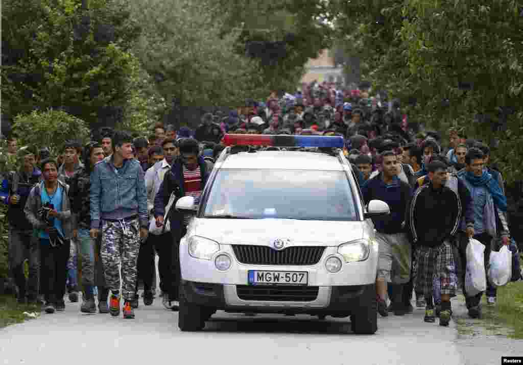 A police vehicle leads migrants as they walk towards the Austrian border from Hegyeshalom, Hungary. Prime Minister Viktor Orban&#39;s chief of staff said the European Union migrant quota system approved in Brussels is &quot;seriously flawed&quot; and Hungary is considering challenging the decision in court.