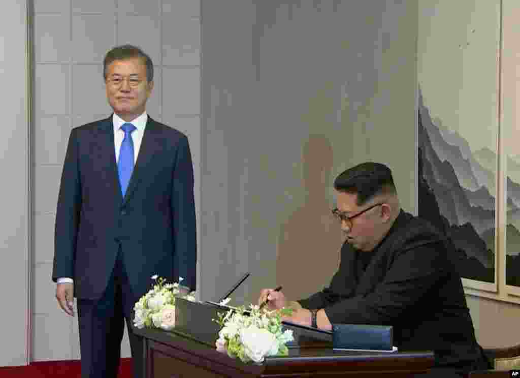 In this image made from video provided by Korea Broadcasting System (KBS), North Korean leader Kim Jong Un signs a guest book watched by South Korean President Moon Jae-in, left, inside the Peace House at the border village of Panmunjom in the Demilitariz