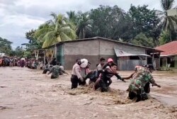 Tentara dan polisi membantu warga melintasi jalan banjir di Malaka Tengah, provinsi Nusa Tenggara Timur, Senin, 5 April 2021. (Foto: AP/video grab)