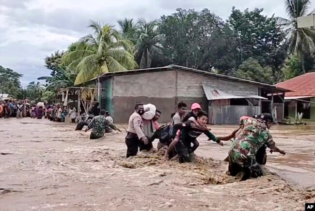 Tentara dan polisi membantu warga melintasi jalan banjir di Malaka Tengah, provinsi Nusa Tenggara Timur, Senin, 5 April 2021. (Foto: AP/video grab)