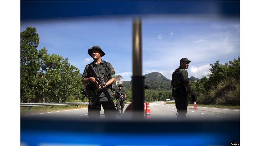 FILE - Members of the General Operations Force control the checkpoint on the road near the area where the abandoned human trafficking camp was discovered in the jungle close to the Thailand border at Bukit Wang Burma in northern Malaysia May 28, 2015.