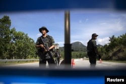 FILE - Members of the General Operations Force control the checkpoint on the road near the area where the abandoned human trafficking camp was discovered in the jungle close to the Thailand border at Bukit Wang Burma in northern Malaysia May 28, 2015.