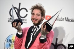 Post Malone poses in the press room with the awards for favorite male pop/rock artist and favorite rap/hiphop album for "Beerbongs & Bentleys" at the American Music Awards, Oct. 9, 2018, in Los Angeles.