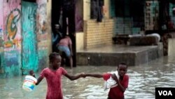 2 anak berjalan dalam air akibat banjir di Haiti, di khawatirkan penyakit Kolera yang menyebar ke luar daerah Artibonite berasal dari air.