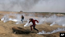 Palestinian protesters run for cover from teargas fired by Israeli troops during a protest at the Gaza Strip's border with Israel, April 13, 2018. 