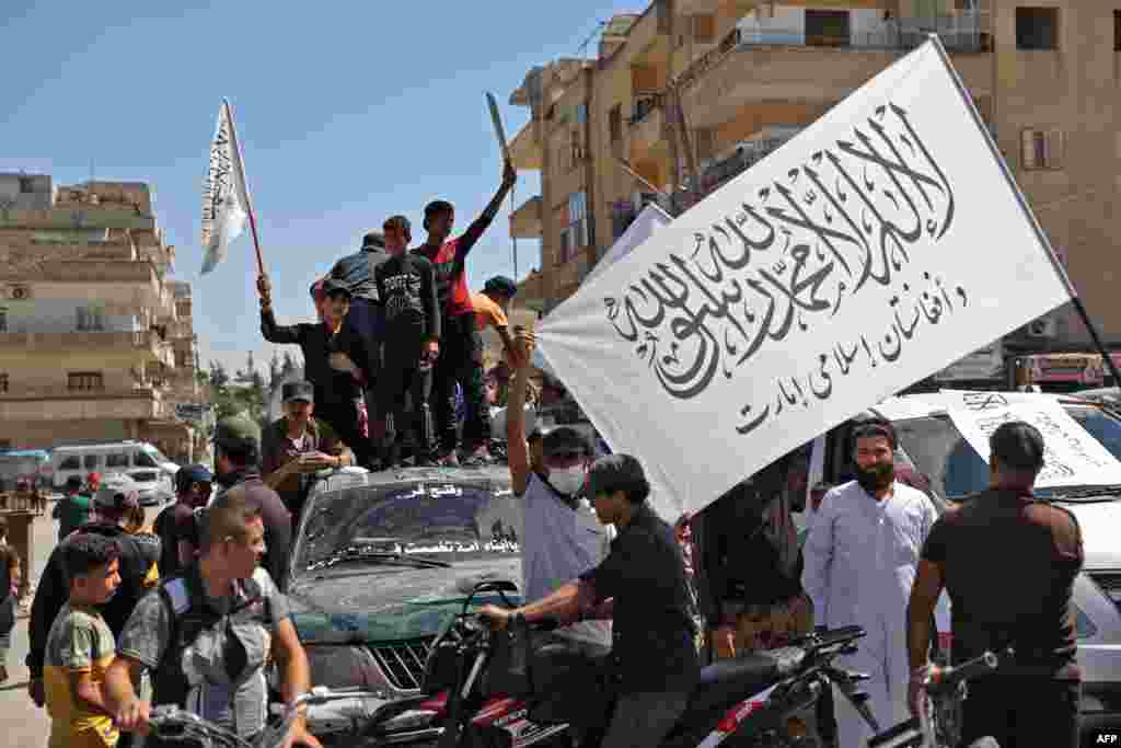 Members of Syria&#39;s top jihadist group the Hayat Tahrir al-Sham alliance, led by al-Qaida&#39;s former Syria affiliate, parade with their flags and those of the Taliban&#39;s declared &quot;Islamic Emirate of Afghanistan&quot; through the rebel-held northwestern city of Idl