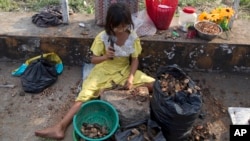 A girl uses a hammer to crack open shells for edible seeds to sell as snacks in Yangon, Myanmar, Nov. 1, 2018. A United Nations report says some 486 million people are malnourished in Asia and the Pacific, and progress in alleviating hunger is stalling.