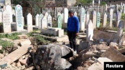 FILE - A man looks down at an unexploded barrel bomb dropped by forces loyal to Syria's President Bashar al-Assad at a cemetery in the al-Qatanah neighbourhood of Aleppo March 27, 2014.