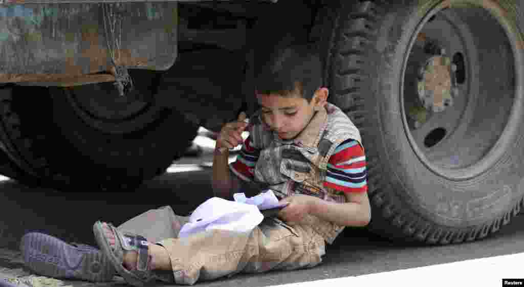 A boy sits near a wheel of a transport vehicle to memorize his lessons on Siteen Road in Sana'a, Yemen.