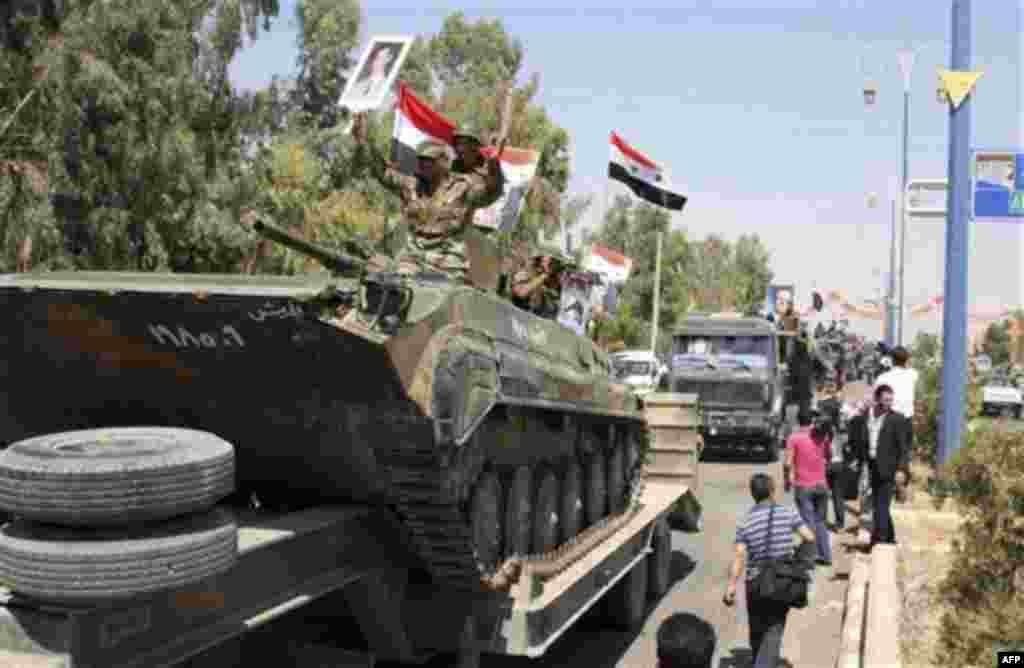 In this photo taken on a government-organized tour, Syrian soldiers atop armored personnel carrier cheer on their way out of the eastern city of Deir el-Zour, Syria, Tuesday, Aug. 16, 2011. State-run news agency SANA said army units began withdrawing from