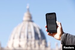 Seorang pria menunjukkan aplikasi 'Click to Pray', aplikasi smartphone yang dirancang untuk memungkinkan umat berdoa dengan sekali klik, di dekat Lapangan Santo Petrus di Vatikan, 19 Oktober 2021. (REUTERS/Guglielmo Mangiapane)