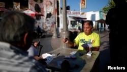 FILE - Men play cards in Mariachi Plaza in the Boyle Heights area of Los Angeles, home to many Mexican and Central American migrants, Aug. 9, 2014. Seven men have been charged in firebombings that drove blacks from their homes in the neighborhood.