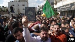 A mourner holds the Koran, Islam's holy book, in front of Palestinians carrying the body of one of five Palestinians who were killed by Israeli security forces following attempted stabbing attacks, during their funeral procession in the West Bank town of 