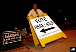 Maricopa County elections official Deborah Atkins places a "vote" sign outside a polling station prior to its opening, Nov. 6, 2018, in Phoenix.