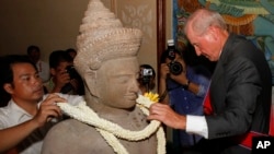 Walter Timoshuk, right, president of Norton Simon Museum of Art in Pasadena, California, places flowers onto a 10th century Cambodian sandstone statue returned from the United States during a handover ceremony at the Council of Ministers in Phnom Penh, Ju