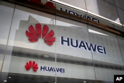FILE - The logos of Huawei are displayed at it retail shop window reflecting the Ministry of Foreign Affairs office in Beijing, Jan. 29, 2019.