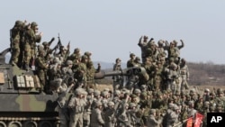 韩国军人和美国军人2012年3月15日在抱川附近地区举行的年度军事演习期间的一次实弹演习之后举手欢呼