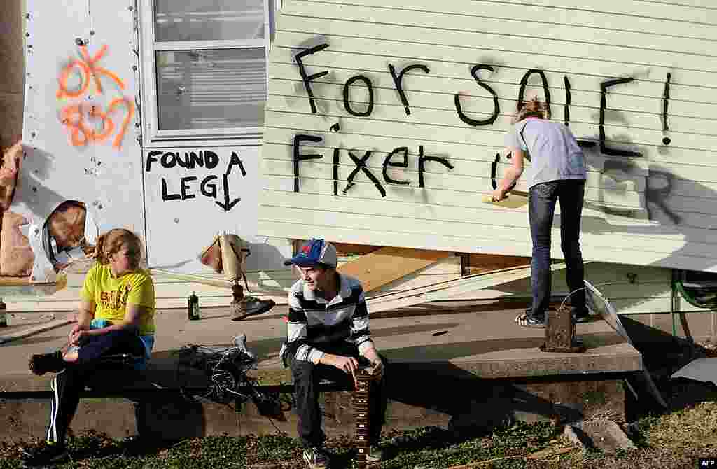 Children sit on the front porch as Lindsey Murray, 15, of Harrisburg, Illinois paints "for sale fixer upper" on the side of the home of their grandmother that was destroyed in a tornado. February 29, 2012. (AP) 