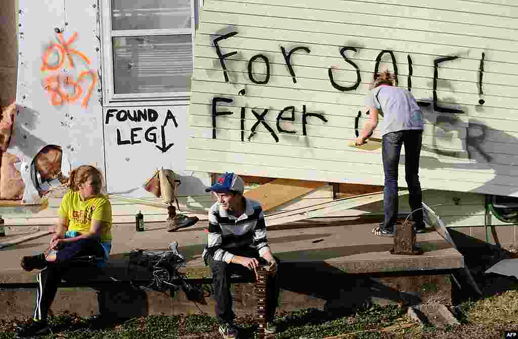 Children sit on the front porch as Lindsey Murray, 15, of Harrisburg, Illinois paints "for sale fixer upper" on the side of the home of their grandmother that was destroyed in a tornado. February 29, 2012. (AP)