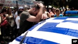 A striking municipal police officer reacts as he leans on a car with a Greek flag during a protest, against new austerity cuts that will affect thousands of public sector workers, in Athens, July 12, 2013.