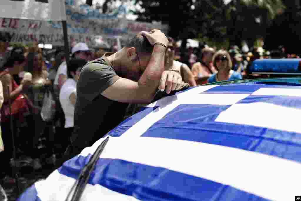 A striking municipal police officer reacts as he leans on a car with a Greek flag during a protest, against new austerity cuts that will affect thousands of public sector workers, in Athens. The government has committed to firing 15,000 people by the end of 2014 and transferring another 12,500 to new positions this year.