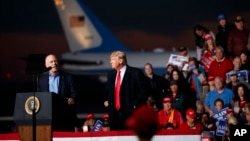Dân biểu Greg Gianforte phát biểu trong khi Tổng thống Donald Trump đứng bên cạnh trong một buổi tập hợp vận động tranh cử cho ông Gianforte tại nhà chứa máy bay Minuteman, ngày 18 tháng 10, 2018, ở Missoula, Montana.