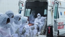 Health workers sitting in an ambulance watch contractual health workers in personal protective suits holding placards during a protest at the Nesco Jumbo COVID-19 center in Mumbai, India Monday, July 5, 2021. (AP)