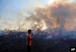 Seorang petugas pemadam kebakaran berbicara melalui walkie talkie saat ia dan timnya memadamkan kebakaran lahan gambut di sebuah lapangan di Pemulutan, Sumatra Selatan. (Foto: AP)