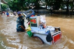 Seorang penjaja kaki lima mendorong gerobak makanannya melewati jalanan yang terendam banjir setelah hujan deras di Jakarta, Sabtu, 20 Februari 2021. (Foto: Ajeng Dinar Ulfiana)