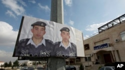 FILE - Two posters with pictures of Jordanian pilot Lt. Muath al-Kaseasbeh hang on a street pole, in front of the pilot's tribal gathering place, in Amman, Jordan,