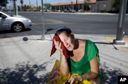 FILE - A woman wipes her face with a cold wet towel to cool off while working outside in Las Vegas, July 1, 2014.