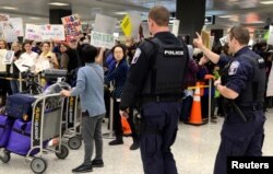 FILE - Police direct arriving passengers past dozens of pro-immigration demonstrators who cheer and hold signs at Dulles International Airport, to protest President Donald Trump's travel ban in Chantilly, Virginia, in suburban Washington, Jan. 29, 2017.