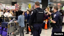 Police direct arriving passengers past dozens of pro-immigration demonstrators who cheer and hold signs at Dulles International Airport, to protest President Donald Trump's travel ban in Chantilly, Virginia, in suburban Washington, Jan. 29, 2017.