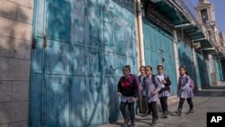 Palestinian children walk past closed souvenir shops, at the tourists market adjacent to the Church of the Nativity, in the West Bank city of Bethlehem, Tuesday, Nov. 16, 2021. (AP Photo/Nasser Nasser)