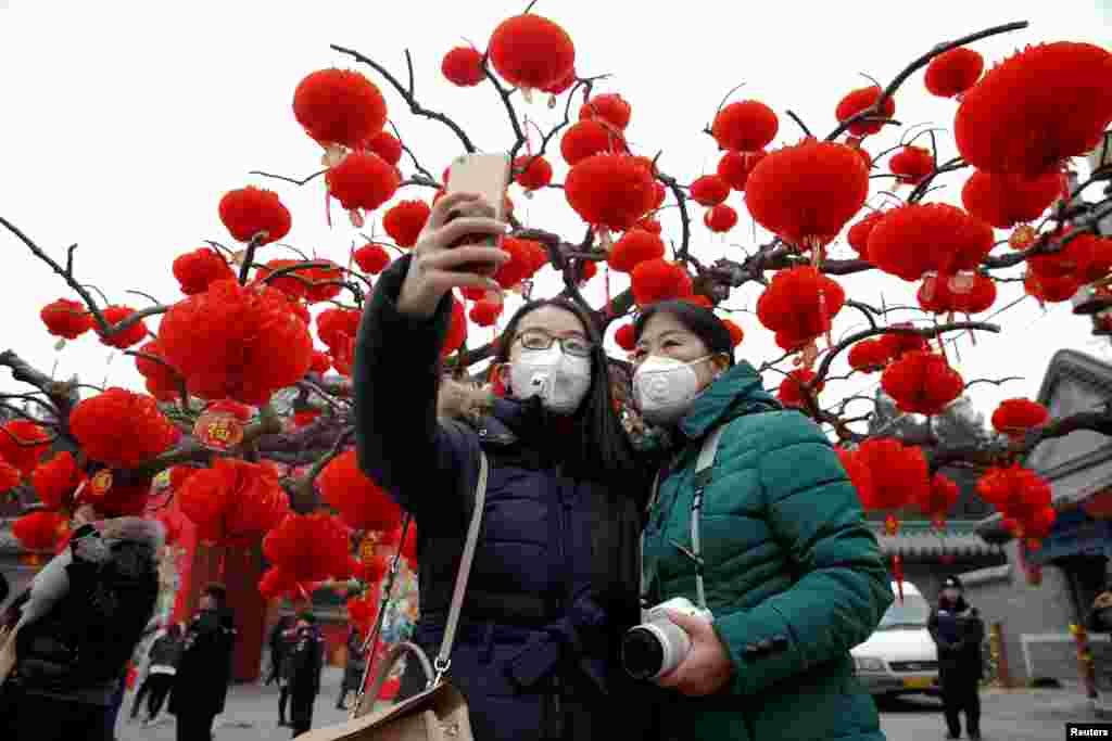 Para pengunjung Kuil Ditan Park yang memakai masker anti-polusi mengambil swafoto di tengah perayaan datangnya Tahun Baru Imlek di Beijing (28/1). (Reuters/Damir Sagolj)