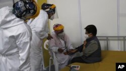Un médico revisa los signos vitales de una anciana luego de ser inoculada con una dosis de la vacuna Pfizer COVID-19 como parte del período de observación, en el centro de convenciones convertido en sitio de vacunación, en Quito, Ecuador, el miércoles 31 de marzo de 2021.