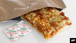 A slice of prototype pizza, in development to be used in MRE's — meals ready to eat, sits in a packet next to a smaller packet known as an oxygen scavenger, left, at the U.S. Army Natick Soldier Research, Development and Engineering Center, Feb. 6, 2014, in Natick, Mass. (AP Photo/Steven Senne)