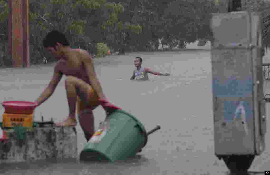 Seorang pria berusaha menyelamatkan barang-barangnya di Quezon City, sementara seorang lainnya berusaha menyeberangi air banjir (7/8).