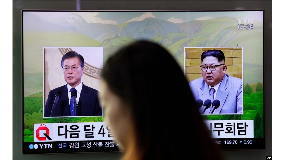 A woman walks past a TV screen showing file footage of South Korean President Moon Jae-in, left, and North Korean leader Kim Jong Un, right, during a news program shown at the Seoul Railway Station in Seoul, South Korea, March 29, 2018.