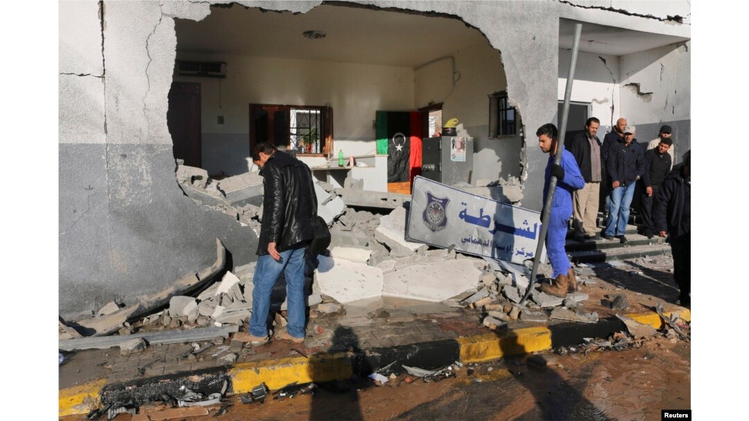 FILE - Civilians and security personnel stand at the scene of an explosion at a police station in Tripoli, Libya, a blast later claimed by militants professing loyalty to Islamic State, March 12, 2015.