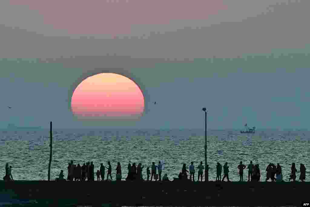 People walk along the seafront as the sun sets near Haji Ali mosque in Mumbai, India.