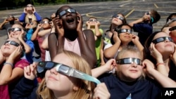 In this photo taken Friday, Aug. 18, 2017, fourth graders at Clardy Elementary School in Kansas City, Mo. practice the proper use of their eclipse glasses in anticipation of Monday's solar eclipse.