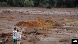 A couple with missing relatives look at the flooded area, after a dam collapsed in Brumadinho, Brazil, Jan. 26, 2019. An estimated 300 people were still missing and authorities expected the death toll to rise during a search made more challenging by rain.