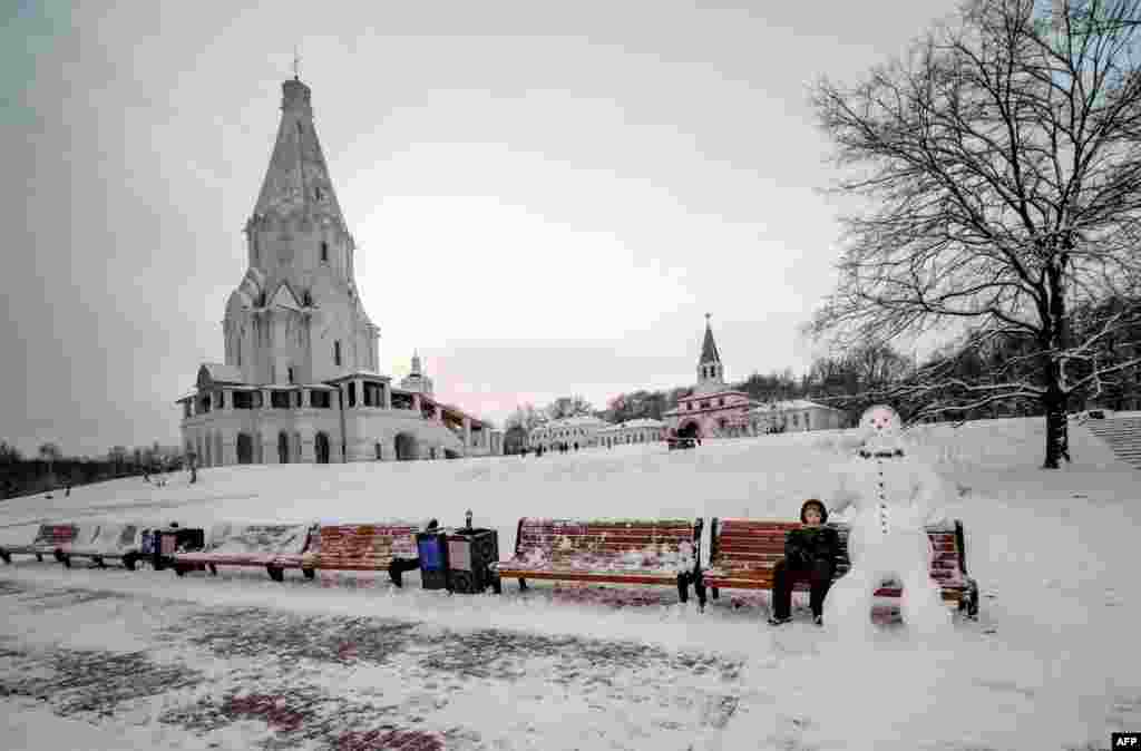 A boy sits next to a snowman in Kolomenskoye park in Moscow, Russia.